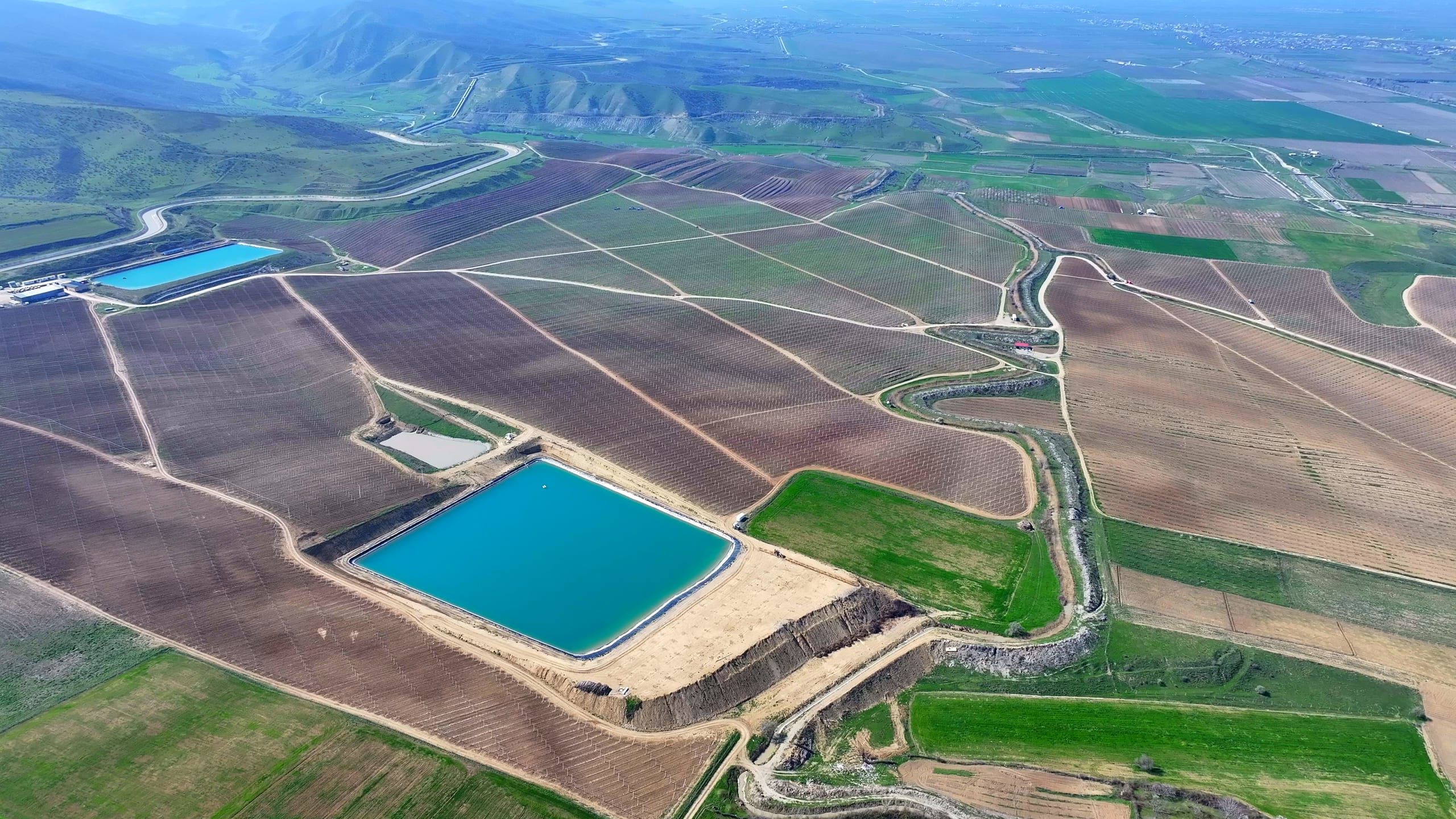 Drone view over the Akofruits irrigation reservoir and orchards, with the Greater Caucasus on the horizon